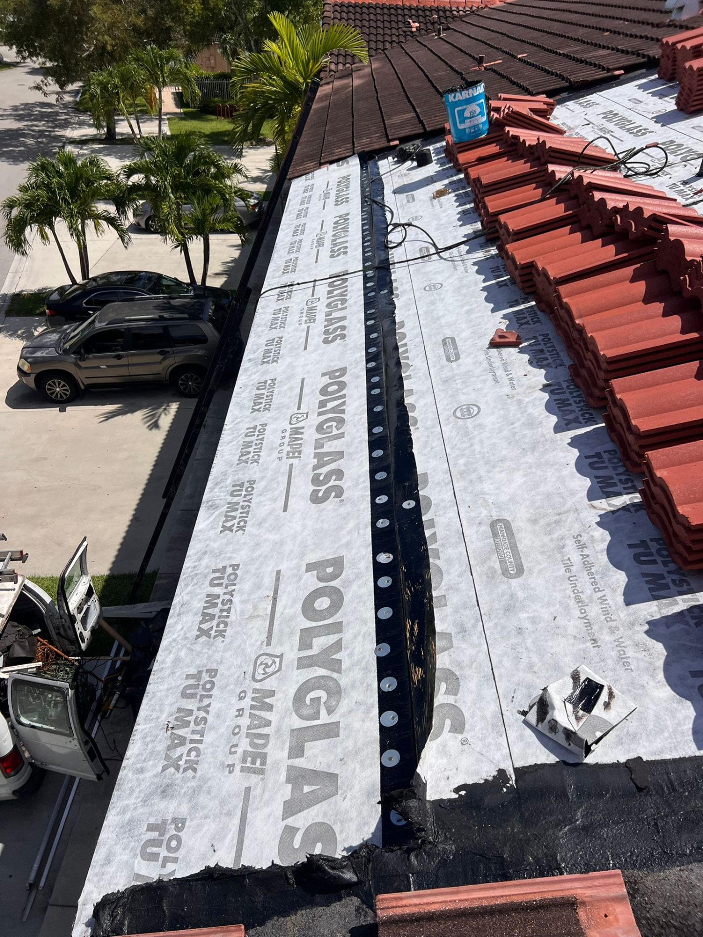 Underlayment exposed beside red tile roofing with mature trees near the Palm Beach Gardens property